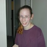 Smiling Nerdy Girl in Glasses with Cumshot on Her Face is a picture of a young girl, wearing glasses and smiling. She has cumshot across her face, and her t-shirt is covered with washed-out spots of old sperm.