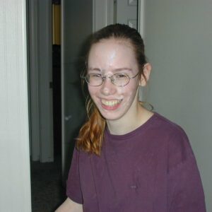 Smiling Nerdy Girl in Glasses with Cumshot on Her Face is a picture of a young girl, wearing glasses and smiling. She has cumshot across her face, and her t-shirt is covered with washed-out spots of old sperm.